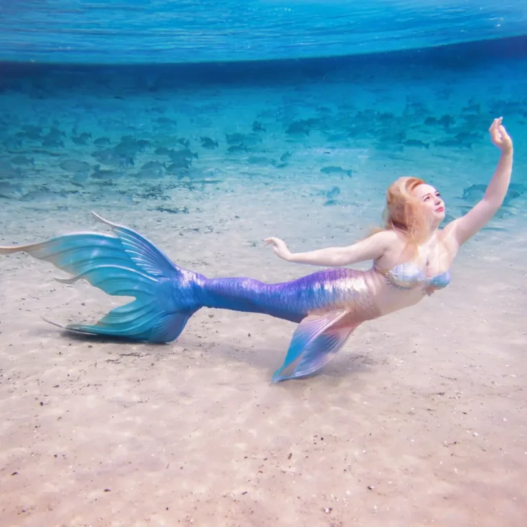 "Artistic underwater image of a mermaid gracefully floating in clear blue water, photographed by Shannon Scott during a Mermaid Retreat. Her expression is peaceful, embodying self-discovery and feminine strength."
