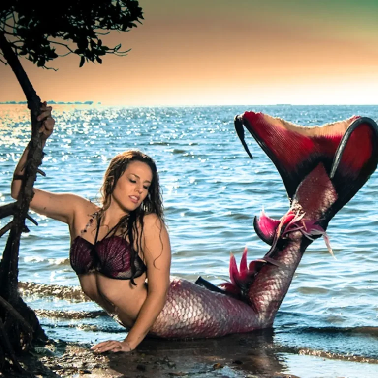 Professional mermaid Shannon Scott sits gracefully on the shore during a creative healing retreat at a Florida beach, bathed in golden light.