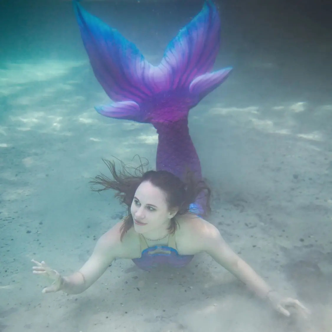 Underwater photo of a graceful mermaid in motion, captured by Shannon Scott. Flowing hair and shimmering tail surrounded by ethereal blue light, evoking magic, freedom, and creative awakening.