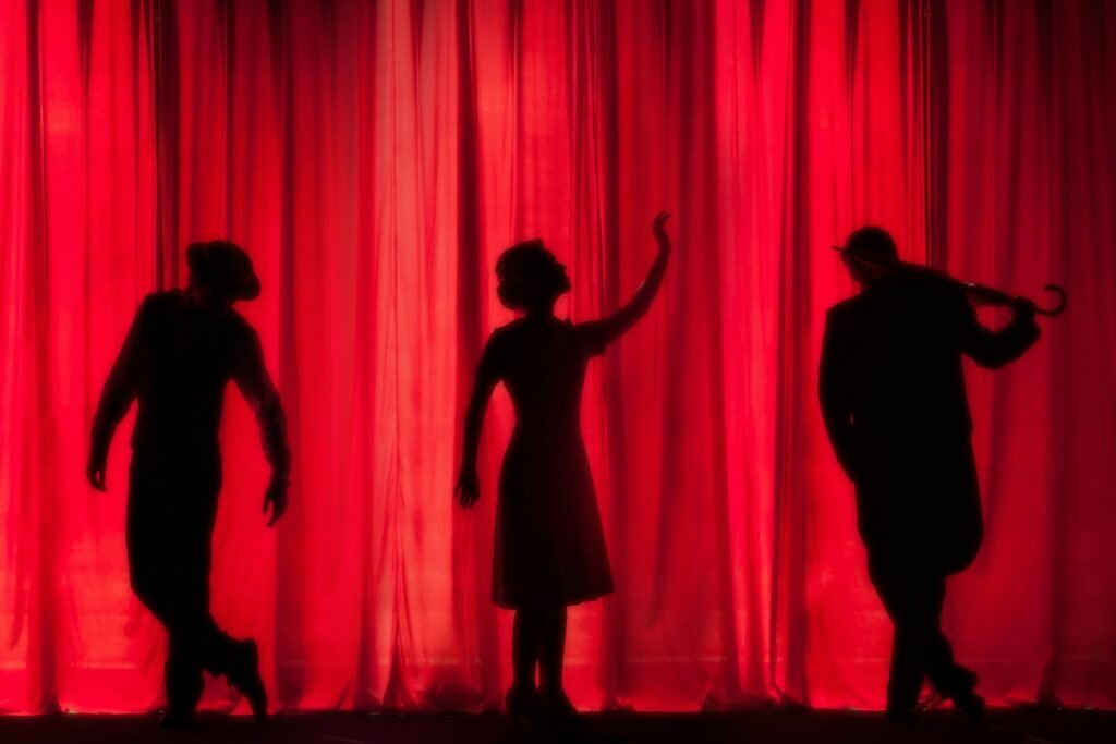 Silhouette of three actors standing near a red curtain, representing creative growth in acting.
