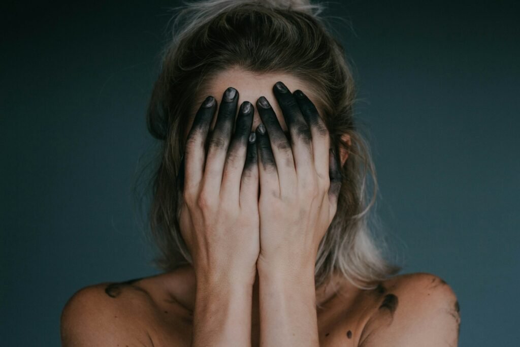 A woman covering her face with black-painted fingers, representing artistic burnout and creative exhaustion.