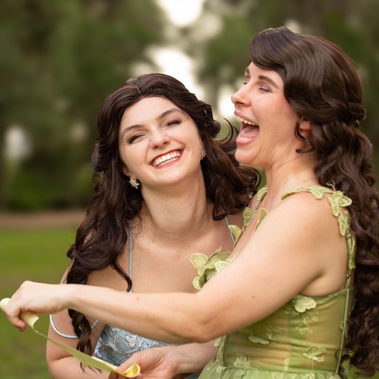 Two women in fairy-inspired lace gowns laughing joyfully together outdoors