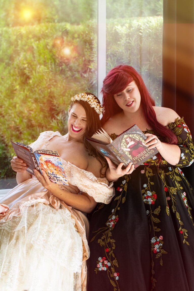 Shannon and Jackie sitting together reading books in an elegant room, both dressed in formal attire, smiling and relaxed.